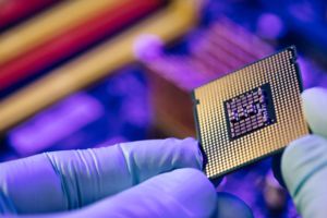 A HAND IN A PROTECTIVE PURPLE GLOVE HOLDS A SEMICONDUCTOR CHIP