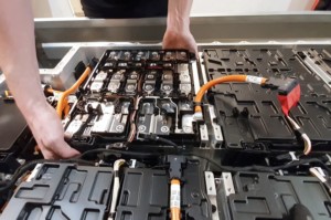 Close-up of a mechanic's hands disassembling an electric car battery on top of a trailer inside a mechanic shop