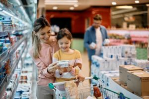 A WOMAN AND A GIRL, SMILING, EXAMINE THE LABEL ON A FOOD ITEM IN A SUPERMARKET AISLE