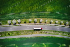 An overhead view of a white and red semi-truck driving on a rode alongside green grass fields