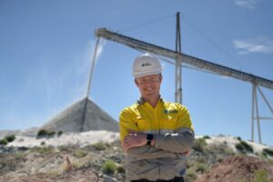 Dale Henderson, chief executive officer of Pilbara Minerals, stands in front of a digger pouring minerals into a pile