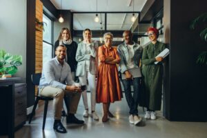 A DIVERSE TEAM OF BUSINESS PEOPLE GATHER FOR A GROUP PHOTO IN A SUNNY OFFICE