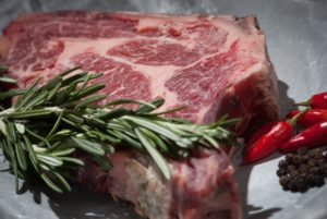 A RAW STEAK SITS ON A COUNTER SURROUNDED BY HERBS AND SPICES