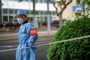 A MAN WEARING A MASK AND OVERALLS STANDS IN FRONT OF A HAZARD TAPE BLOCKING A STREETy-1396385585.jpg