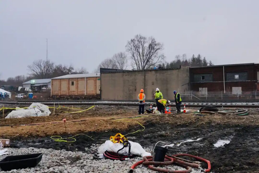 FOUR PEOPLE CAN BE SEEN WORKING ON THE TRAIN DERAILMENT CLEAN-UP IN EAST PALESTINE, OHIO.