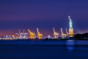 The Statue of Liberty overlooking port Cranes, all lit up, at night