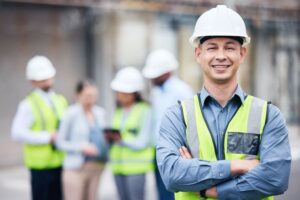 A mature male architect stands with his arms crossed at a building site