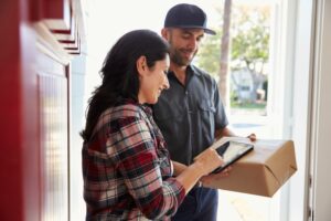 A WOMAN SIGNS FOR A PACKAGE DELIVERY AT HER OPEN FRONT DOOR