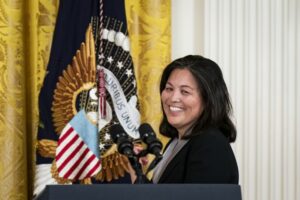 A WOMAN SMILES IN FRONT OF THE PRESIDENTIAL FLAG BEARING AN EAGLE AND THE WORDS E PLURIBUS UNUM