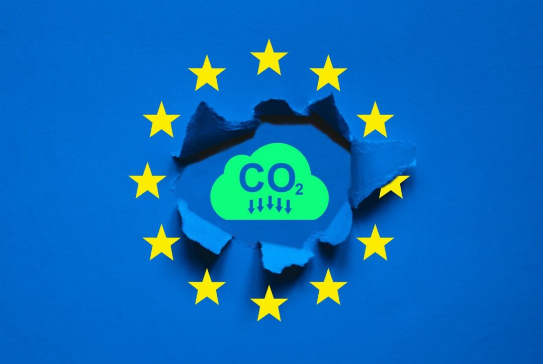 INSIDE THE BLUE AND YELLOW EU FLAG, A HOLE IS RENT, SHOWING THE LETTERS CO2 WITH DOWNWARD ARROWS UNDERNEATH