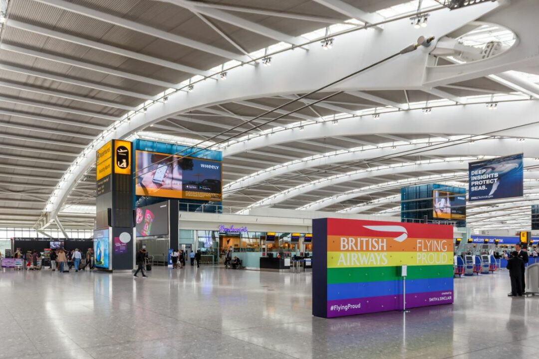 A MODERN AIRPORT TERMINAL WITH ARCHED RIBBED ROOF HOUSES A LARGE SIGN FOR BRITISH AIRWAYS