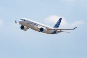 A BLUE AND WHITE PLANE FLIES THROUGH BLUE SKIES