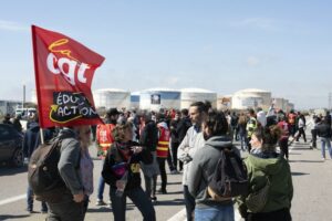 PROTESTORS BEARING A FLAG CLUSTER IN FRONT OF OIL STORAGE TANKS