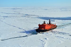 A BRIGHT ORANGE ICE BREAKER VESSEL MAKES ITS WAY THROUGH ICE UNDER HARSH SUN