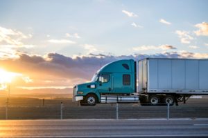 A big rig semi truck driving on the highway road with fields on the sides at sunset