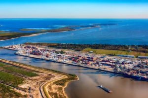 A CARGO SHIP MAKES IT WAY OUT OF THE CHANNEL OF A PORT TOWARD THE OPEN SEAS