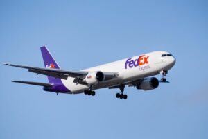 A PLANE WITH FEDEX TAIL INSIGNIA FLIES THROUGH A BLUE SKY