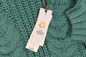 A LABEL ON A DARK GREEN CABLE KNIT SWEATER READS 100% RECYCLED FABRIC