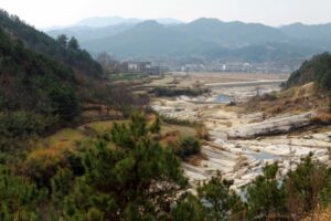 A DRY RIVER VALLEY OPENS OUT INTO FLATLANDS FRINGED BY CITY BUILDINGS