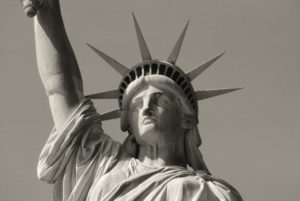 A SEPIA-TINTED BLACK AND WHITE PHOTO OF THE TORSO AND HEAD OF THE STATUE OF LIBERTY