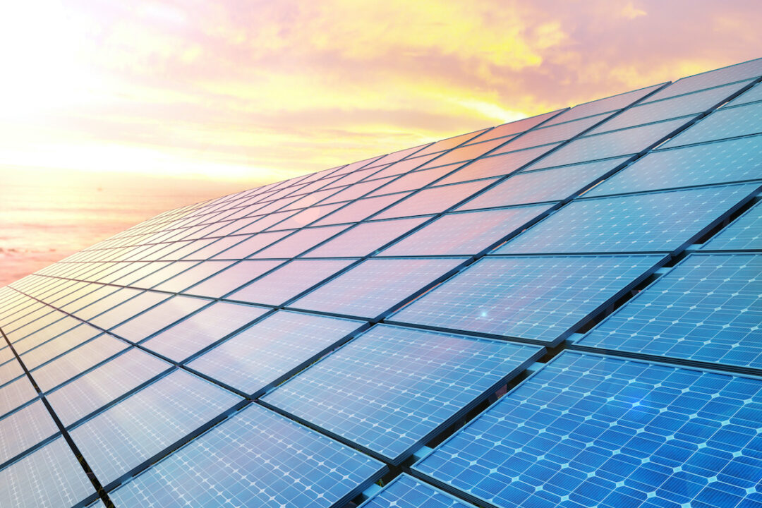 A close-up of solar panels can be seen in front of a sunset. Photo: iStock.com/JONGHO SHIN