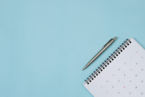 A calendar with a pen above it rests on top of a blue background. Photo: iStock.com/Rattankun Thongbun