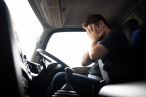 A TRUCK DRIVER IN THE CAB OF A TRUCK HOLDS HIS FACE IN HIS HANDSg