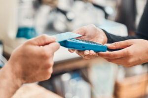 A PERSON'S HAND IS HOLDING A CREDIT CARD OVER A CARD SCANNING DEVICE.