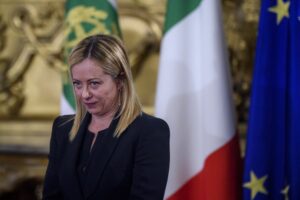 ITALIAN PRIME MINISTER GIORGIA MELONI IS STANDING IN FRONT OF AN ITALIAN FLAG AND AN EU FLAG