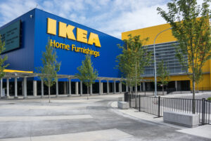 THE EXTERIOR OF A CANADIAN IKEA STORE. A GRAY WALKWAY PEPPERED WITH GREEN TREES LEADS TO THE ENTRANCE OF THE STORE.