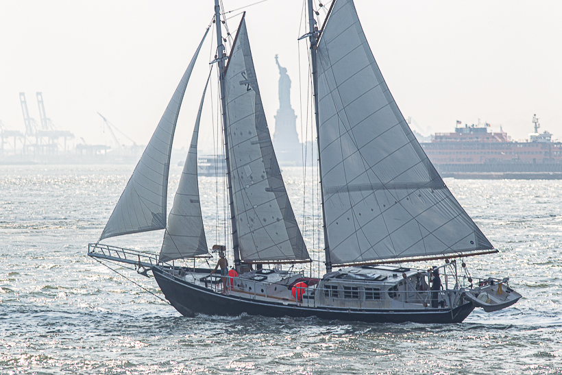 A SCHOONER SAILING BOAT PASSES THE STATUE OF LIBERTY ON A BRIGHT, BREEZY DAY