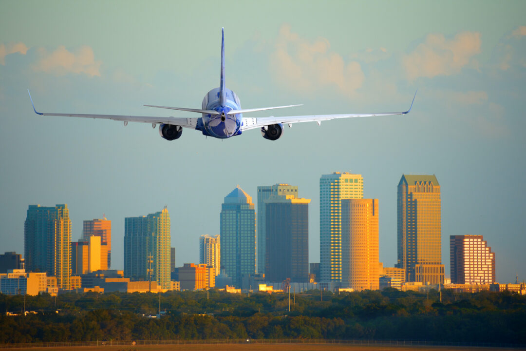 A PASSENGER AIRPLANE IS EITHER ARRIVING AT OR DEPARTING FROM AN AIRPORT WITH A CITY SKYLINE IN THE BACKGROUND ON A CLEAR DAY.