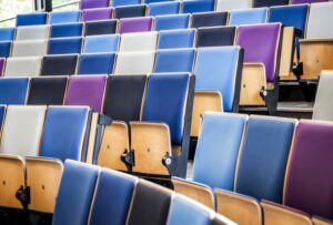 ROWS OF EMPTY BLUE, WHITE, PURPLE AND BLACK SEATS CAN BE SEEN