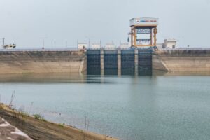 A BODY OF WATER LEADS TO THE OUTSIDE OF A HYDROPOWER PLANT WITH A TOWER CONNECTED THAT HAS THE WORDS "EVN" IN BLUE FOLLOWED BY "HPC TRI AN" IN RED