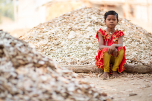 A CHILD SQUATS AMONG MOUNDS OF GLISTENING ROCKS, HER FOREHEAD GLINTING WITH MICA DUST