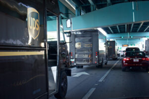 THREE UPS DELIVERY TRUCKS ARE DRIVING IN A BUSY INTERSECTION.