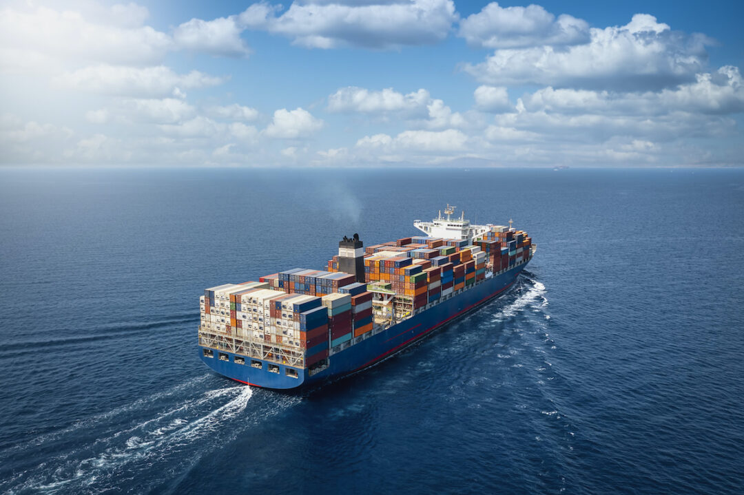 A LARGE CONTAINER SHIP CARRYING MULTI-COLORED CONTAINERS TRAVELS ON A CALM OCEAN.