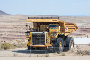 A VINTAGE YELLOW ORE TRANSPORTATION TRUCK SITS IN FRONT OF A MINE.