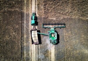 AN AERIAL VIEW OF A COMBINE HARVESTER MOVING THROUGH A BARLEY FIELD. 