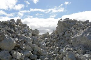 ROCKS SIT IN A STOCKPILE UNDERNEATH A CLOUDY BLUE SKY.