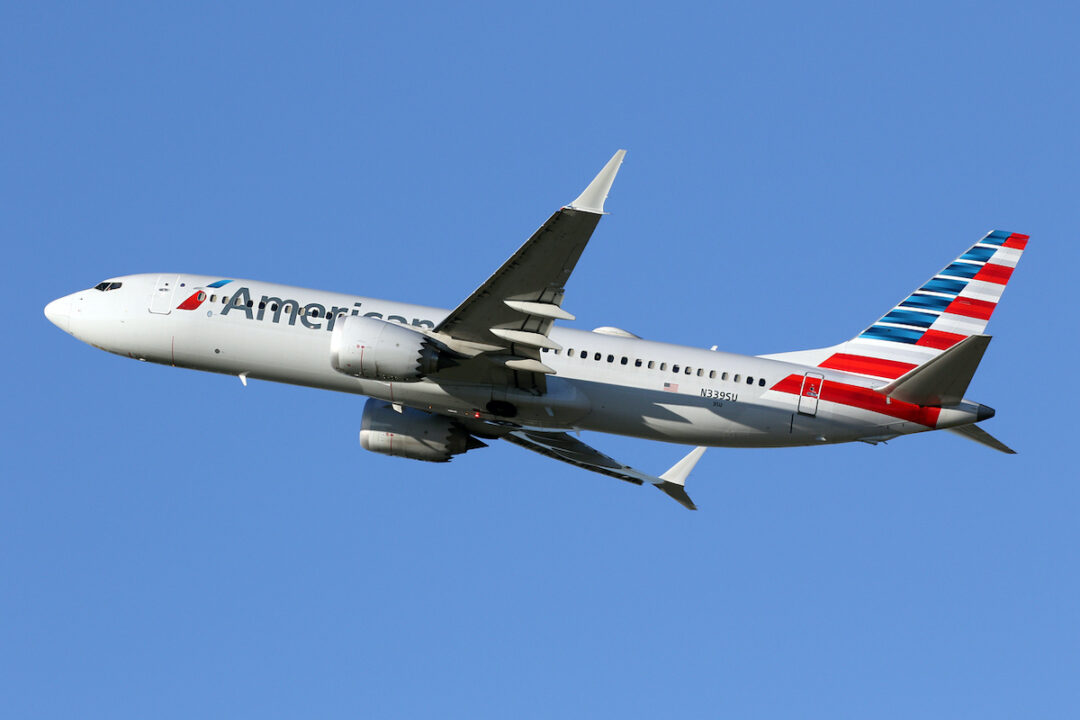 AN AMERICAN AIRLINES PLANE IS FLYING THROUGH A CLEAR BLUE SKY.