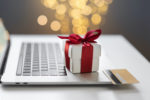 A SMALL WHITE BOX WITH RED WRAPPING ON IT SITS NEXT TO A CREDIT CARD. BOTH ITEMS ARE RESTING ON TOP OF A LAPTOP.