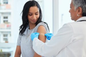 A DOCTOR PLACES A BAND AID ON THE SHOULDER OF A PATIENT.