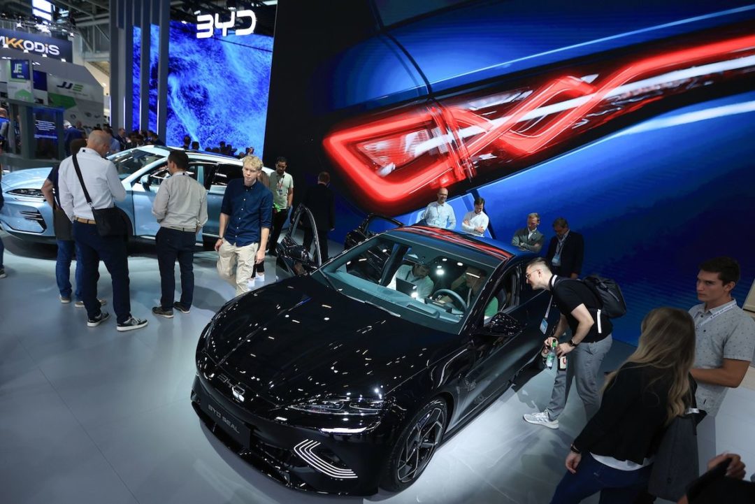 MULTIPLE PEOPLE ARE INSPECTING AN ELECTRIC VEHICLE AT A SHOW.