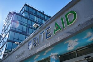 GROUND VIEW OF A RITE AID STORE. A SKYSCRAPER IS IN THE BACKGROUND.