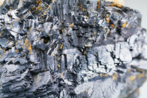 AN EXTREME CLOSE-UP OF A MINERAL ORE. THE DARK GREY ORE FEATURES SOME SMALL PATCHES OF GOLD MATERIALS.