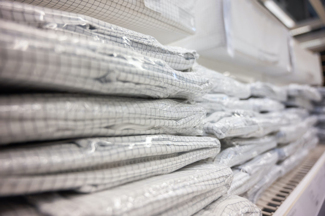 SEVERAL BED LINENS IN PLASTIC PACKAGES ARE STACKED ON TOP OF EACH OTHER ON A SHELF.