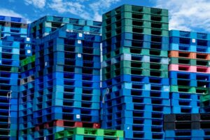 TOWERING PILES OF COLORED PLASTIC PALLETS SIT ON A DOCK