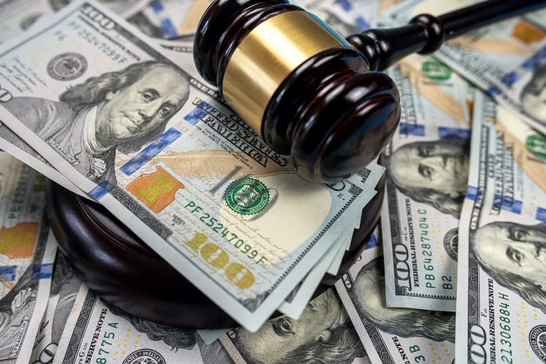 A GOLD AND BROWN WOODEN GAVEL SITS ON TOP OF STACKS OF $100 BILLS.