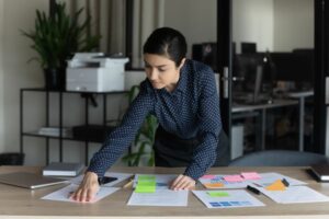 A WOMAN IN A POLKA DOT SHIRT ARRANGES PIECES OF PAPER ON A DESK